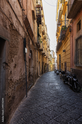 Old narrow alley with parked motorcycles in Italy.