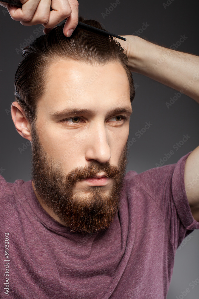 Handsome young bearded guy is caring of his appearance