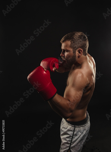 Athletic bearded boxer with gloves on a dark background