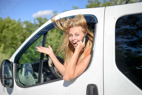 Young blond woman excited and speaking phone in white car