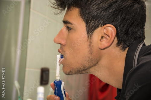 Headshot of young man brushing teeth with toothbrush
