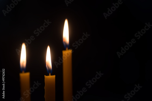 yellow candle lit on black background. photo