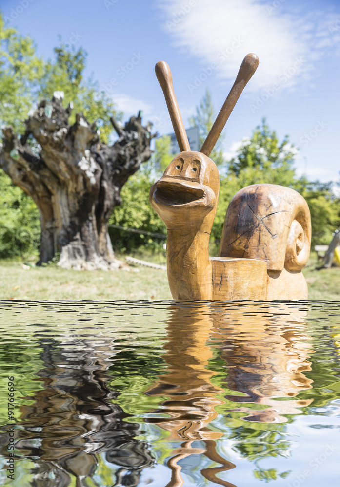 wooden snail toy on the shore of a lake in a park - obrazy, fototapety, plakaty 