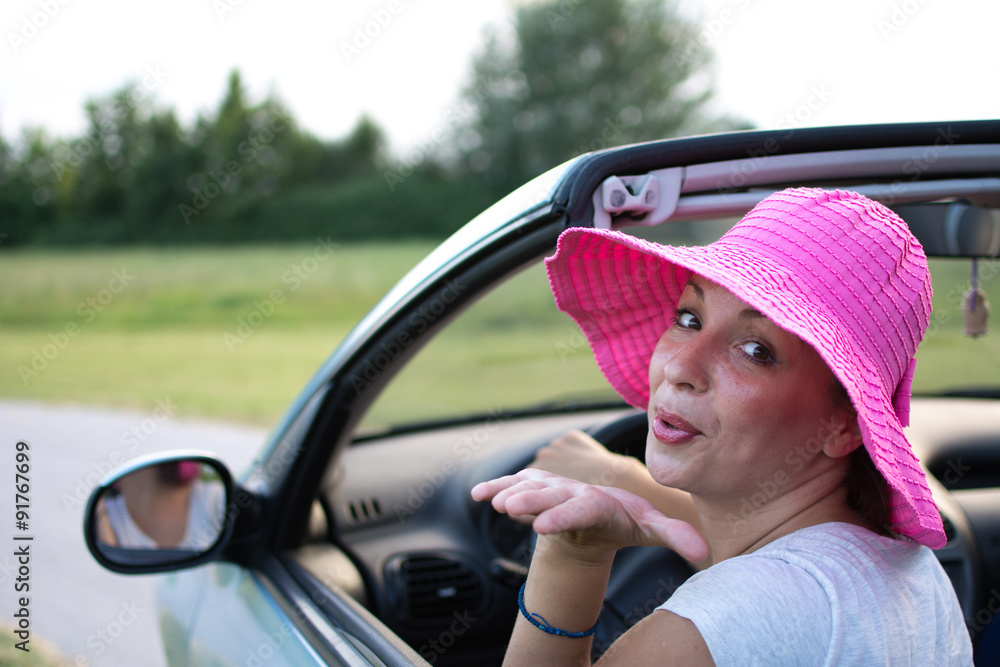 Beautiful young woman in white shirt and pink hat, smiling from a car
Beautiful young woman in white shirt and pink hat, smiling from a car