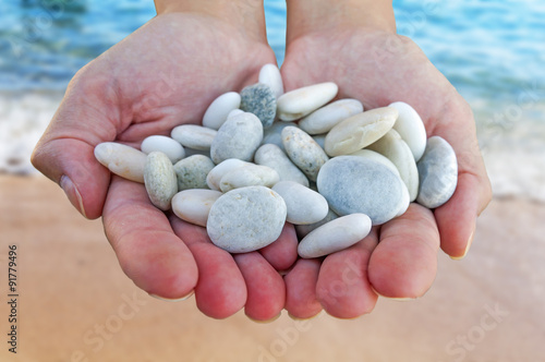 Woman hands holding small stones in hands on beach background