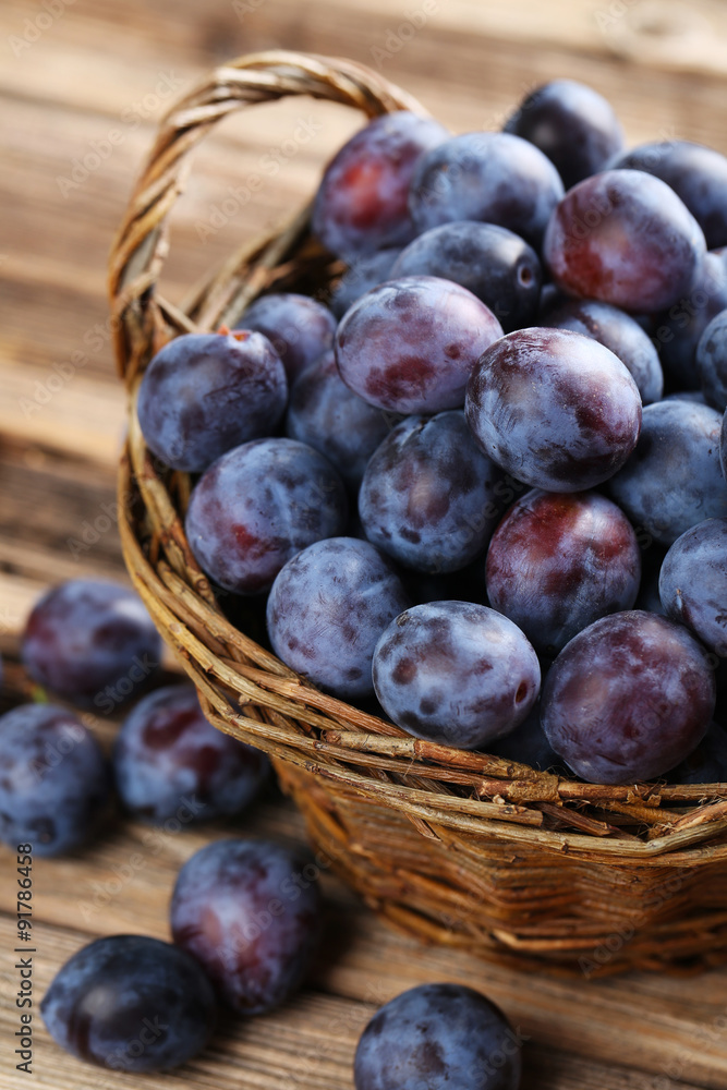 Fototapeta premium Fresh plums in basket on the brown wooden background