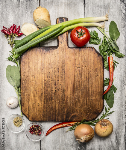 fresh autumn and vegetables seasonings and hearbs around a wooden cutting board on bright, rustic wood background top view