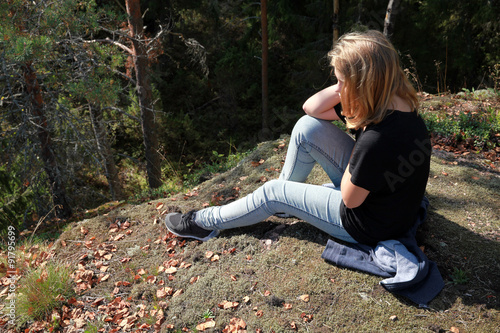 Blond Caucasian teenage girl sits in forest