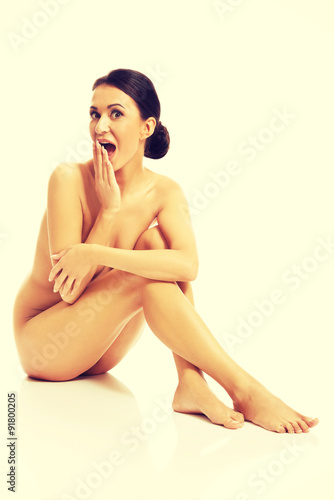 Surprised nude woman sitting on the floor