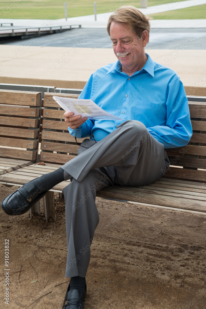 Male sitting on a bench, smiling while reading court documents. Male sitting on a bench, smiling while reading court documents.