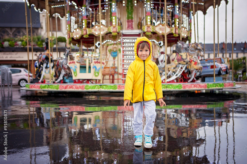 Sweet child, boy watching carousel in the rain, wearing yellow r