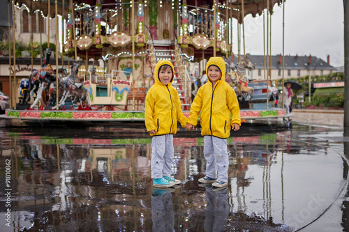 Two sweet children, boy brothers, watching carousel in the rain,