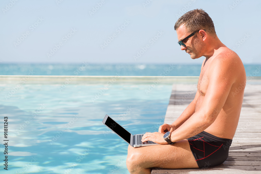 Young man using laptop computer by the pool