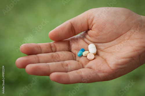 Closeup pills on woman hand on green nature background