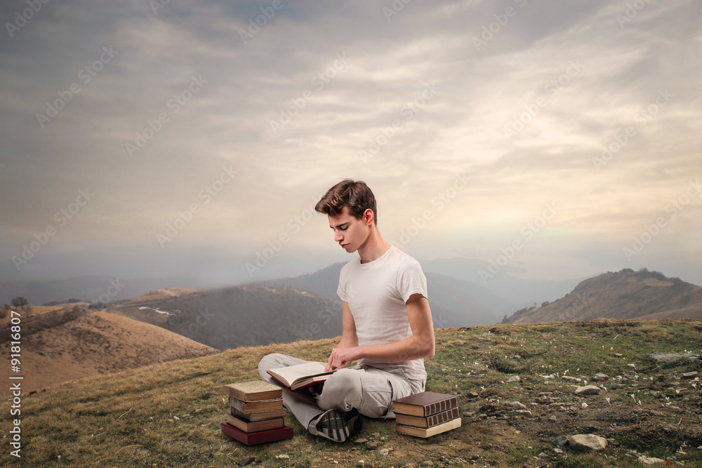 Young man reading books while sitting in the mountains