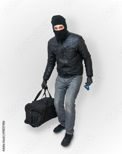 Masked burglar or thief with balaclava is sneaking with black ba