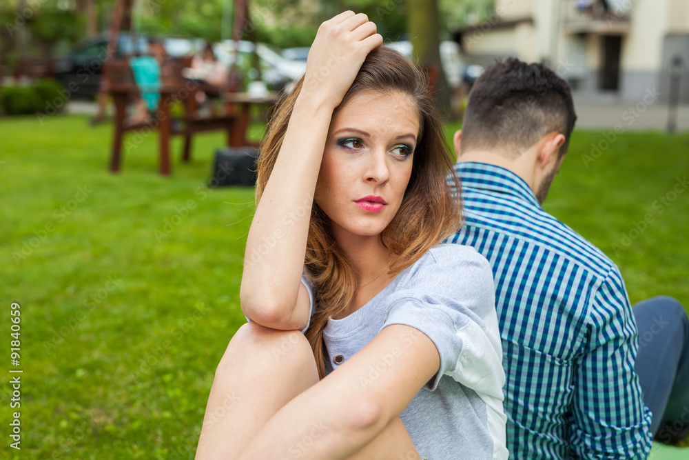 Couple sitting in the garden on the blanket back to back and girl is sad. Couple sitting in the garden on the blanket back to back and girl is sad.