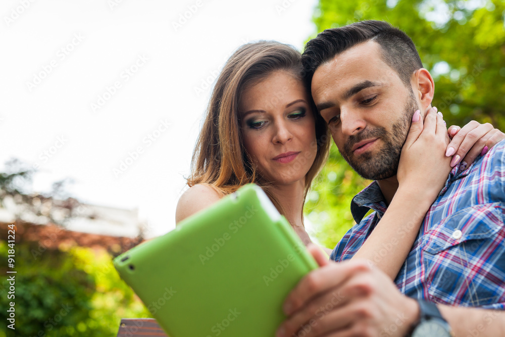 Couple sitting on the bench in the garden, using tablet and smiling. Couple sitting on the bench in the garden, using tablet and smiling.