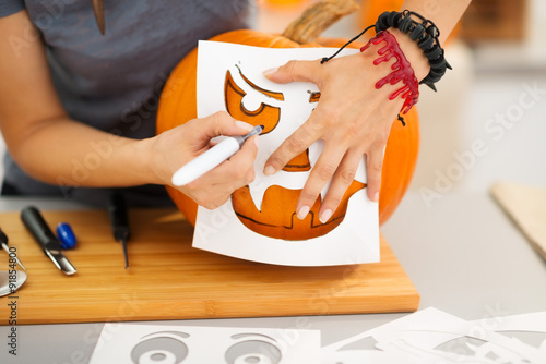Woman using stencils to carve pumpkin Jack-O-Lantern. Closeup