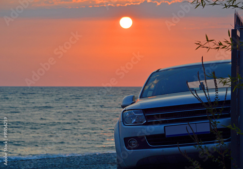 Силуэт автомобиля-внедорожника на фоне заходящего солнца на берегу Черного моря вечером