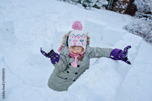 happy child girl playing snowballs in snow castle in winter garden