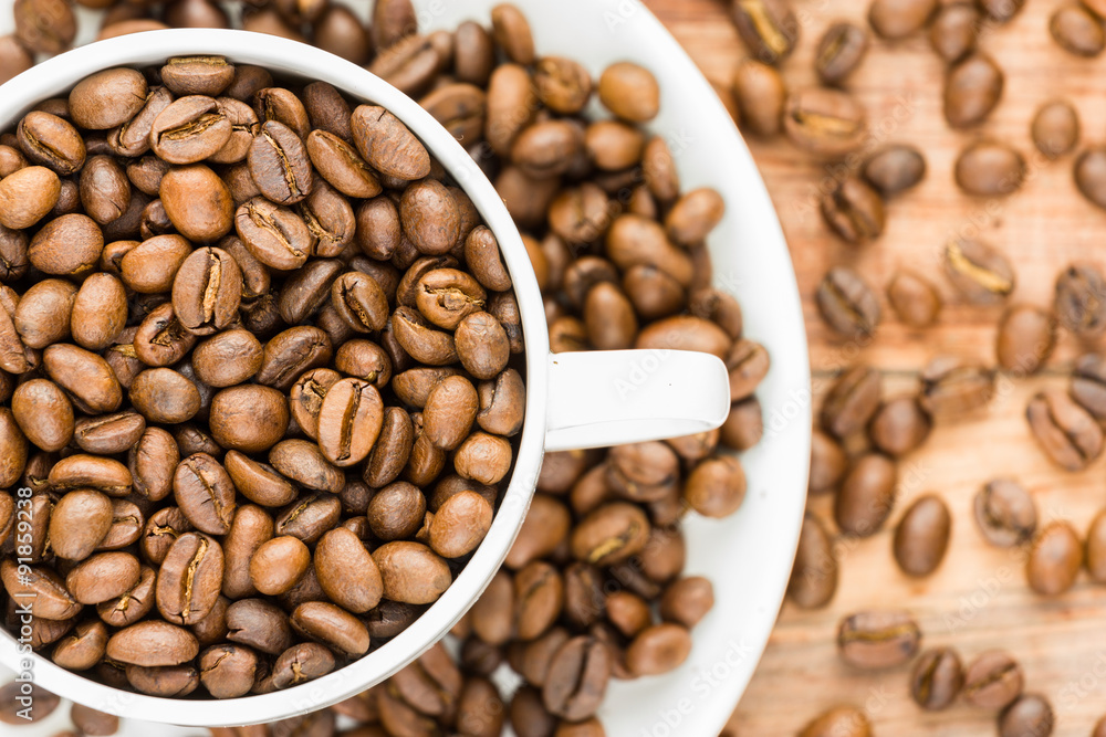 coffee beans inside white half visible cup and plate on wood background
coffee beans inside white half visible cup and plate on wood background