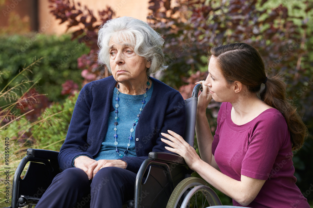Fototapeta premium Adult Daughter Comforting Senior Mother In Wheelchair