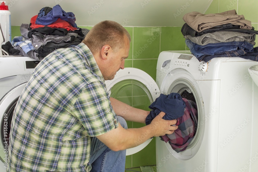 Man washes clothes in the washing machine. Housework men. Man helping his wife when washing clothes. The division of housework. Man Near The Washing Machine.
Man washes clothes in the washing machine. Housework men. Man helping his wife when washing clothes. The division of housework. Man Near The Washing Machine.