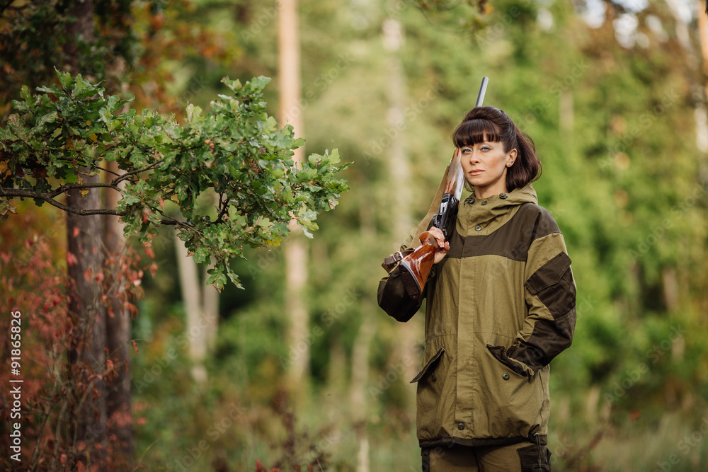 Fototapeta premium Young beautiful woman hunter with a shotgun in the forest