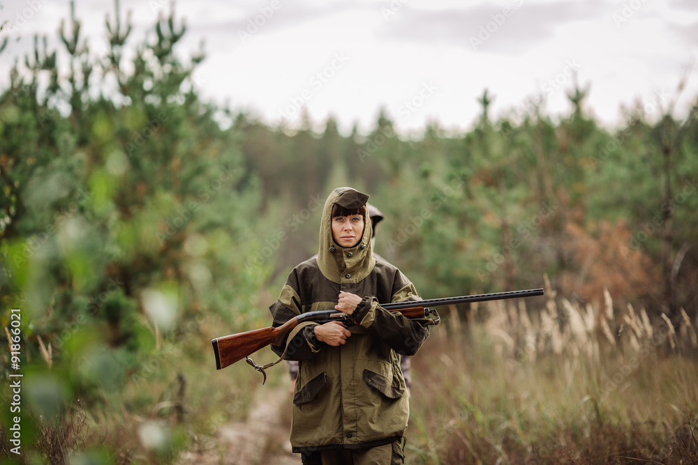 Fototapeta premium Young beautiful woman hunter with a shotgun in the forest