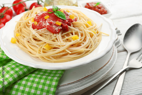 Spaghetti with tomato sauce and cheese on white plate, on color wooden background