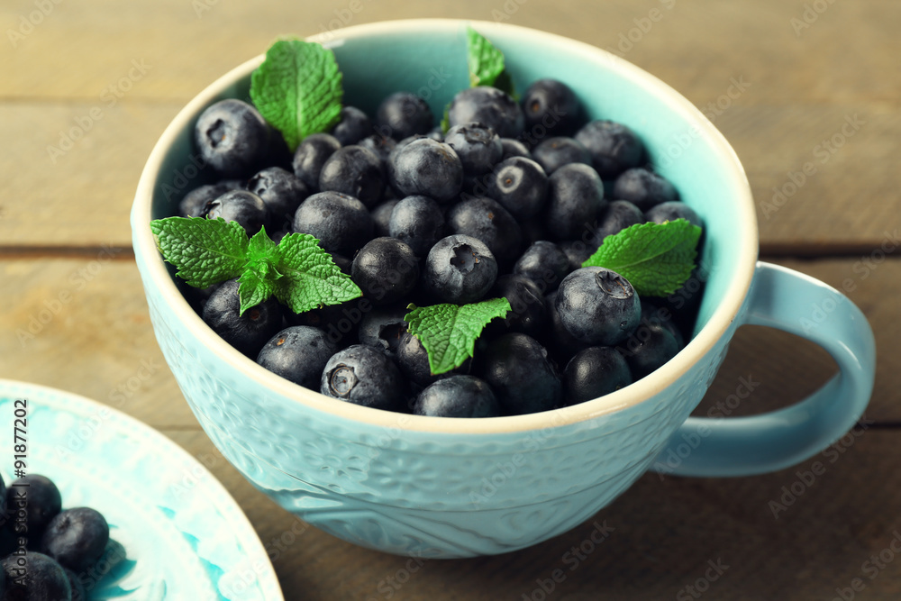 Cup and plate with fresh blueberries on wooden table close up Cup and plate with fresh blueberries on wooden table close up