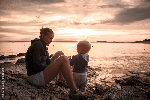 Mother and son sitting on a rocky beach, talking and playing