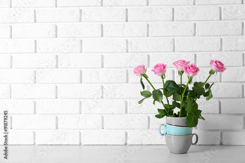 Beautiful roses in stack of cups on brick wall background © Africa Studio