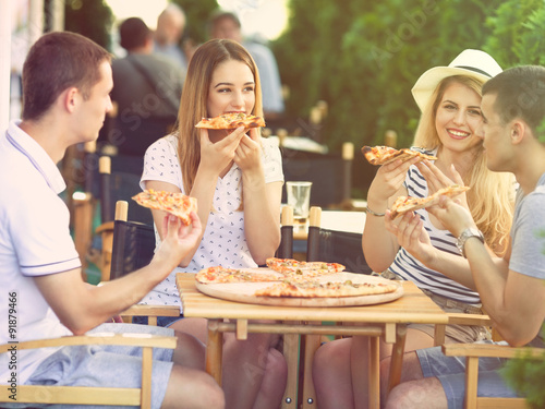 Group of happy young people eating pizza in a restaurant