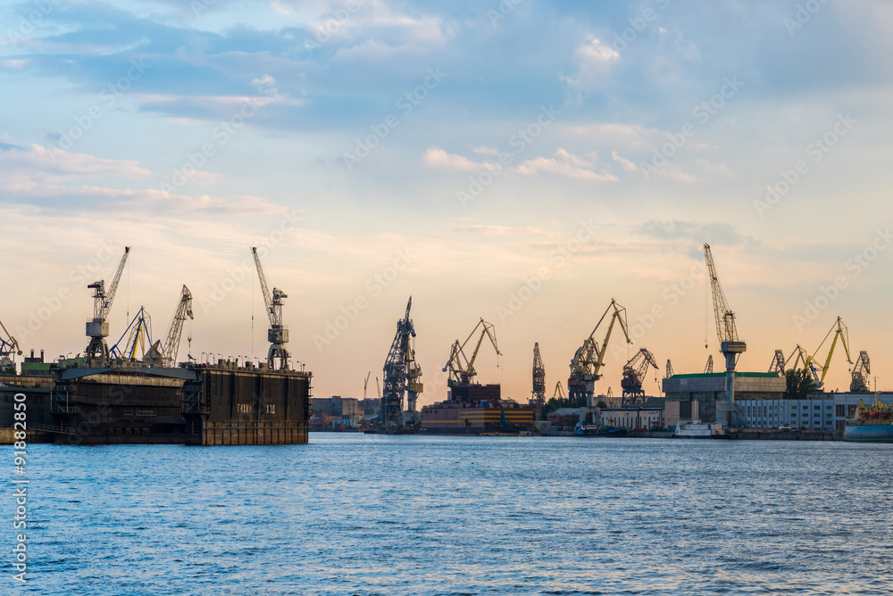 Construction cranes of Saint Petersburg shipyards along the Neva River at sunset