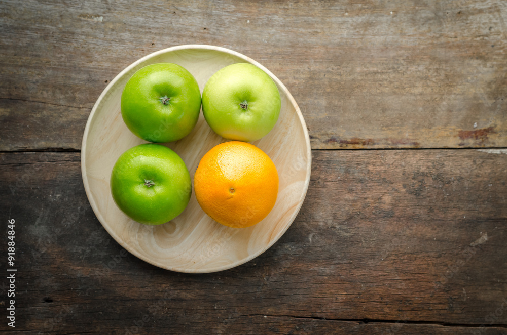 Top view of green apples and orange on wooden plate, fruits on w