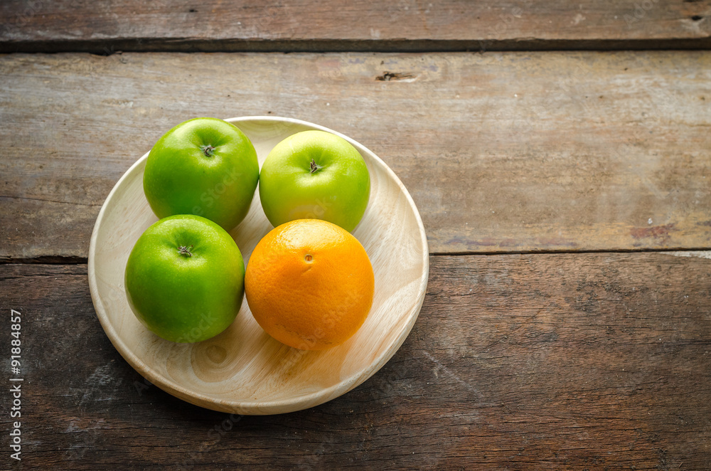 Green apples and orange on wooden plate, fruits on wooden disk Green apples and orange on wooden plate, fruits on wooden disk