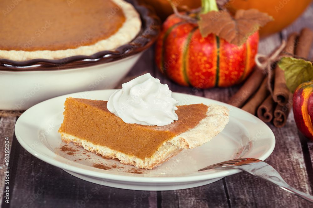 Slice of a pumpkin pie on wooden table. Pie and autumn decorations in the background. Slice of a pumpkin pie on wooden table. Pie and autumn decorations in the background.