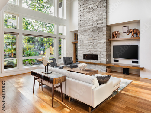 Beautiful living room with hardwood floors, fireplace, and large bank of windows with view of lush vegetation, in new luxury home photo