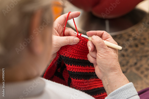 Seniorin häkelt mit roter und schwarzer Wolle