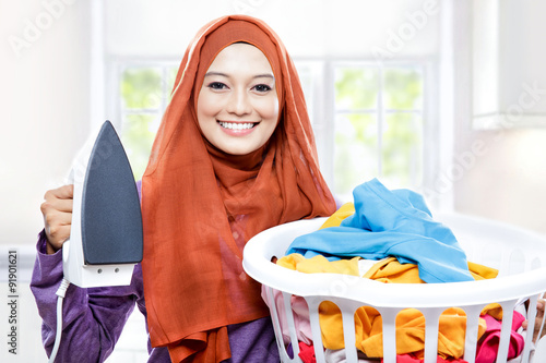 young smiling woman wearing hijab holding iron and carrying laun photo