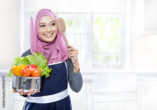 young woman carrying a pan full of vegetables and wooden spatula