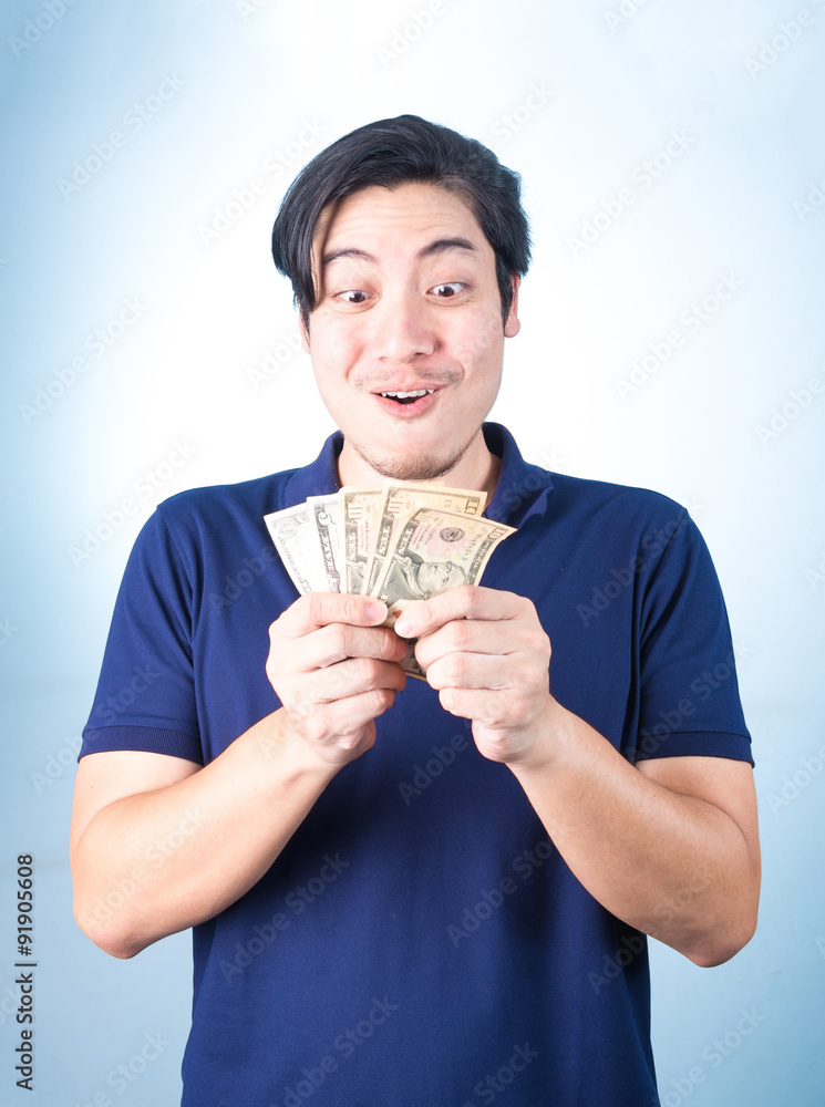 Asian handsome man holding money while standing on blue backgrou Asian handsome man holding money while standing on blue backgrou