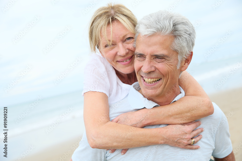 Senior man giving piggyback ride to his wife on the beach