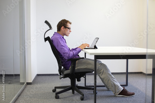 text neck - man in slouching position on ergonomic chair working with tablet at desk photo