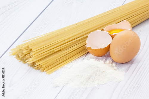 Uncooked spaghetti, flour and eggs on wooden table