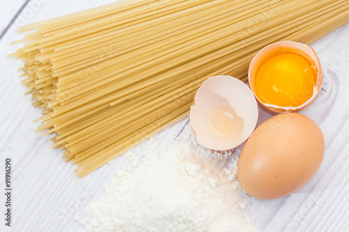Uncooked spaghetti, flour and eggs on wooden table