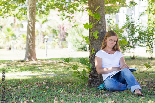 A beautiful blonde woman reading a book in a park © Ravil Sayfullin