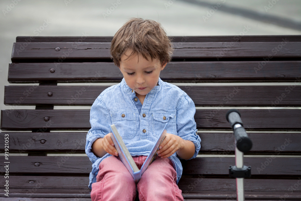 Cute boy, read a book in the park, sitting on bench, summertime Cute boy, read a book in the park, sitting on bench, summertime